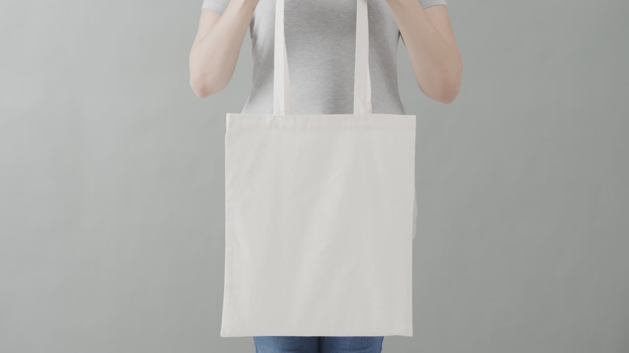 mujer caucásica con una camiseta blanca sosteniendo una bolsa blanca sobre un fondo gris, espacio de copia, cámara lenta