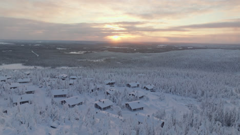 drone flying over a mountaintop cottage town, tilting toward the sunset, winter in lapland