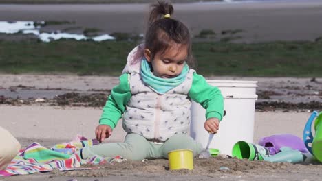 Niño-Pequeño-Jugando-Con-Una-Cuchara-Y-Juguetes-De-Colores-En-La-Playa,-Cámara-Lenta