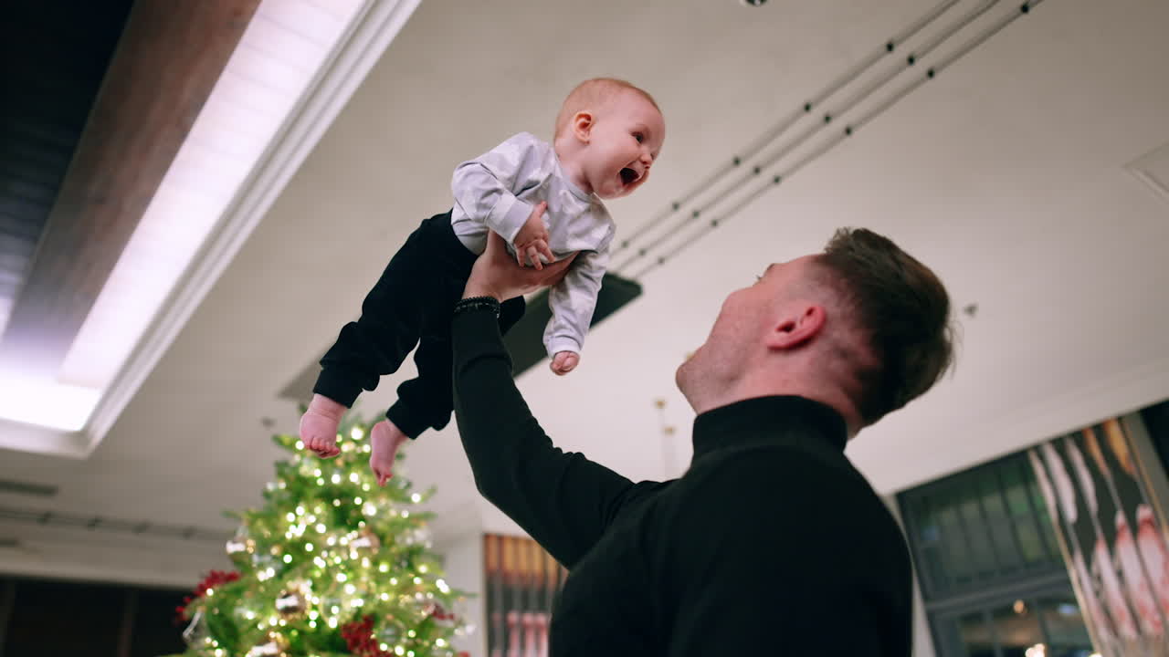 Man in black sweater holding his son over the head. Little child is excited and touches dad's face. Low angle view.