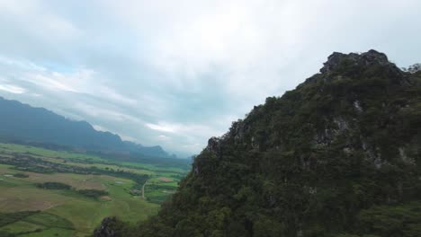 drone soars above the blue lagoon, laos, with green valleys and cliffs under moody overcast skies