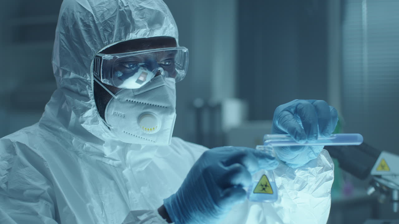 Black Lab Scientist in Protective Uniform Pouring Liquid into Flask