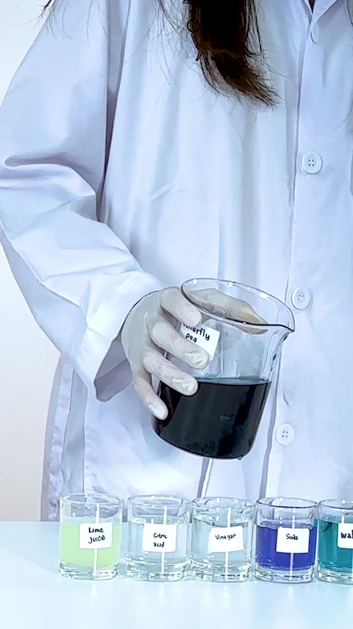 Scientist pours butterfly pea flower solution into pH indicators, observing color changes under bright lighting in a lab setting