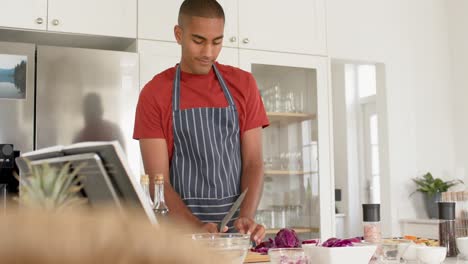 hombre biracial en delantal cortando verduras en la cocina, cámara lenta