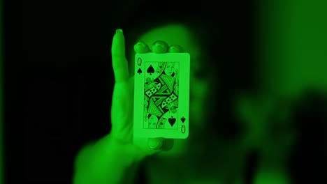 woman extends queen of spades card in front of her under eerie green lighting
