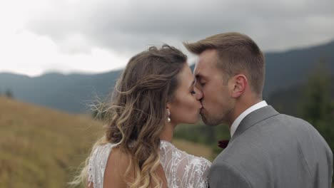 Lovely-young-newlyweds-bride-and-groom-embracing,-making-a-kiss-on-mountain-slope,-wedding-couple