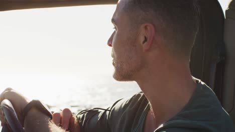 feliz hombre caucásico sentado en el coche disfrutando de la vista en un día soleado junto al mar