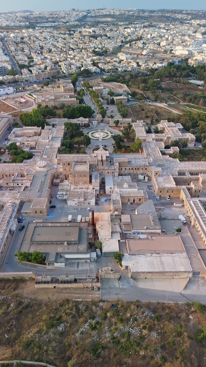 Attard, Malta: Ospedale Mount Carmel, struttura psichiatrica e di salute mentale con storica architettura in pietra maltese, giardini e strade circostanti, in una vista aerea verticale diurna.