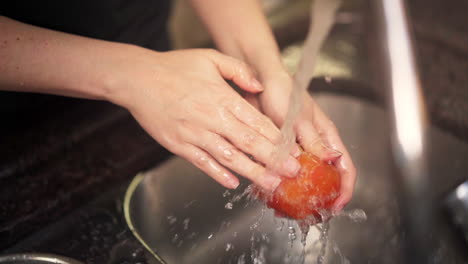 Toma-En-Cámara-Lenta-De-Manos-Femeninas-Lavando-Un-Tomate-Bajo-El-Agua-De-Un-Grifo-De-Cocina