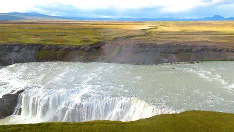 Drohnenverfolgung-Aus-Der-Luft-über-Einer-Großen-Isländischen-Ebene-Mit-Einem-Fluss-Im-Vordergrund-Und-Einem-Großen-Beeindruckenden-Wasserfall-Namens-Golfoss