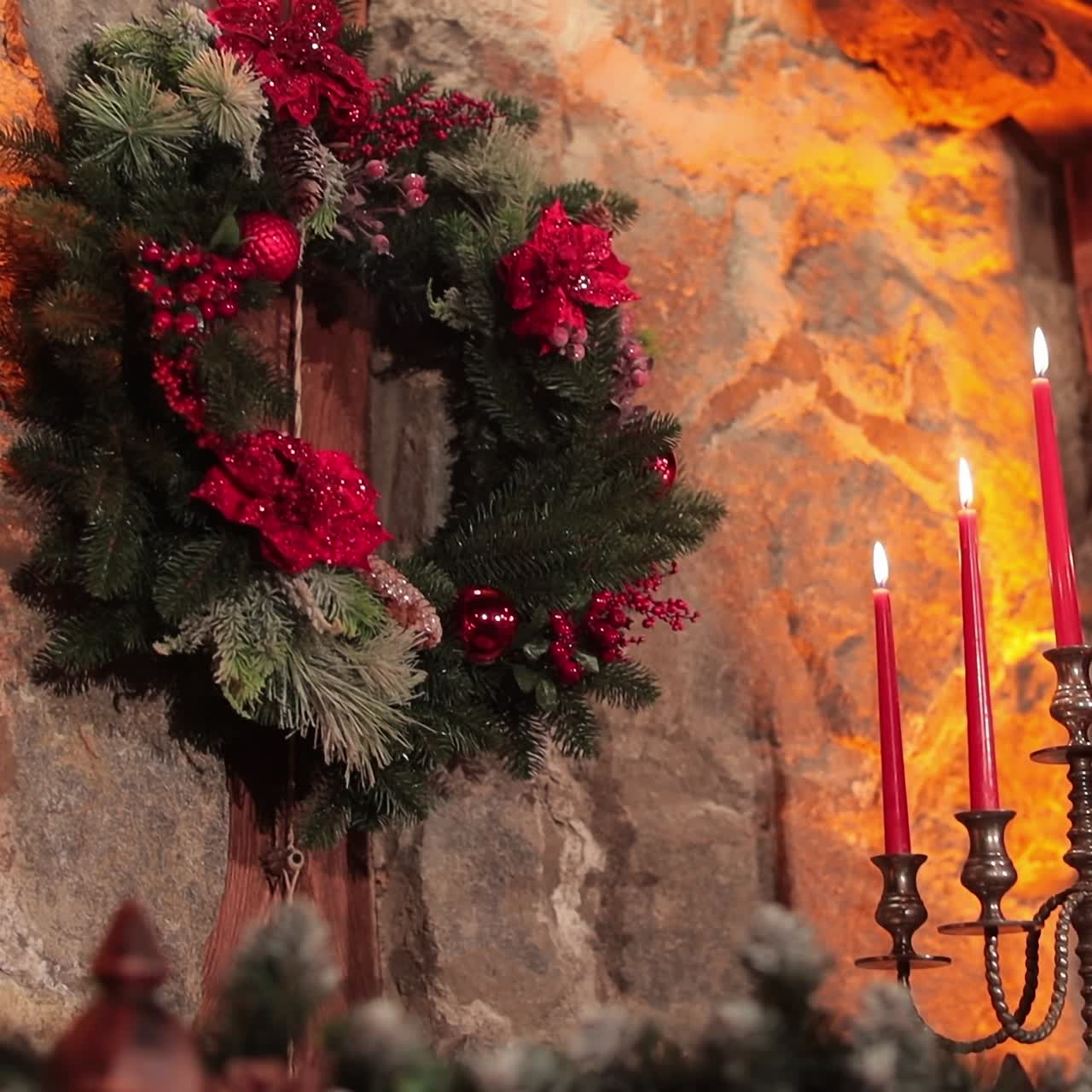 Fir-tree wreath with bright artificial flowers and decorations. Stone wall lit with dim soft light of candles