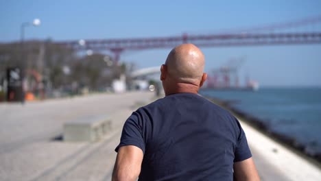 Back-view-of-middle-aged-man-running-at-riverside