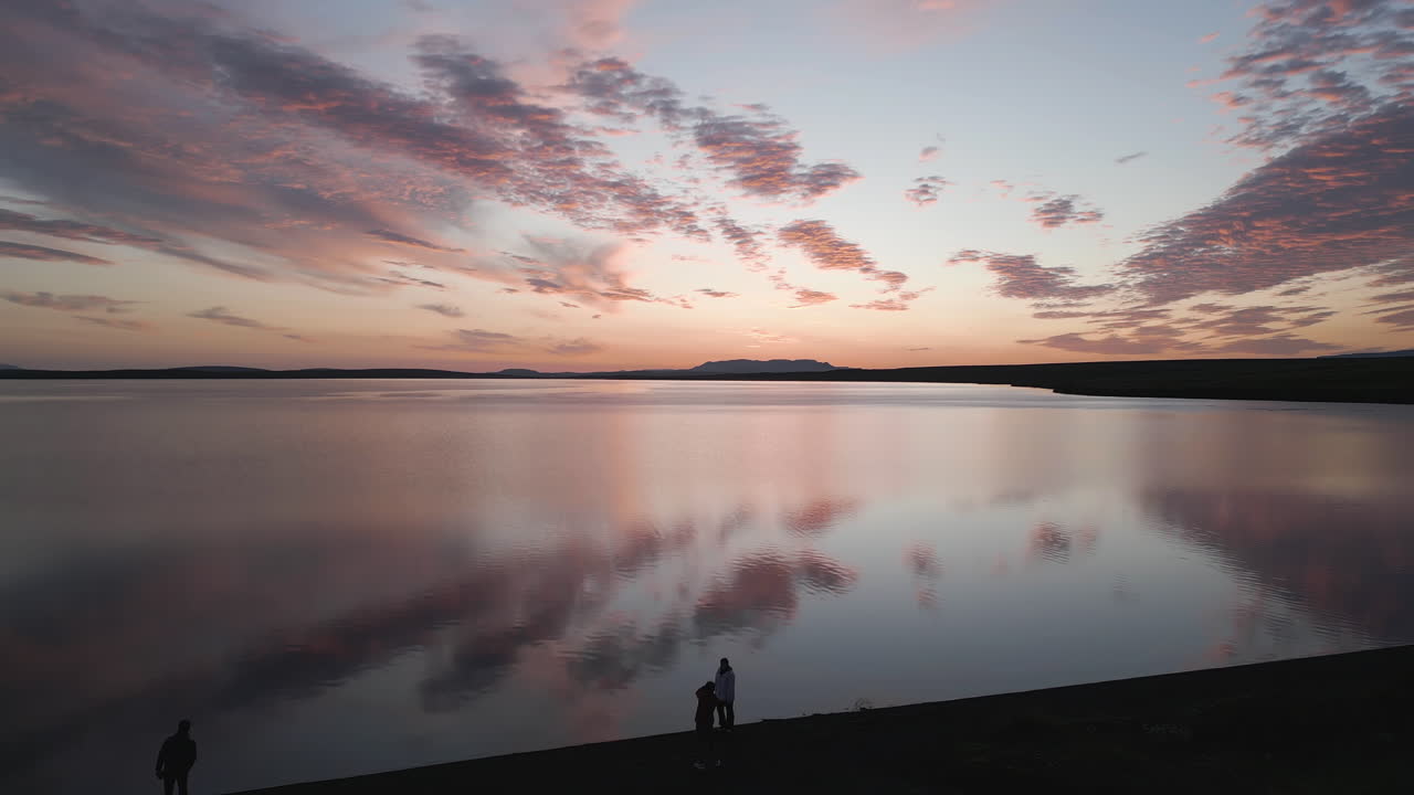 Midnight Sun Glow Reflected On Idyllic Sea With People On The Shores In Iceland. Tilt-down Shot
