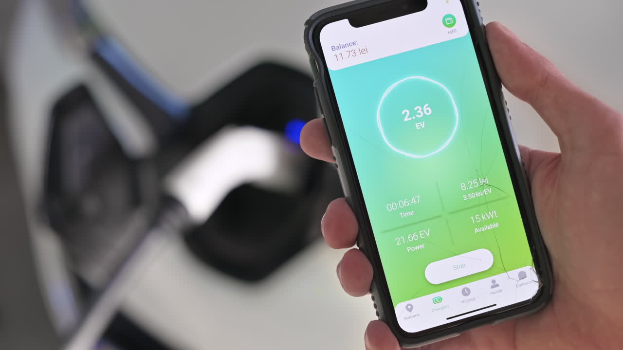 Man charging electro car, holding smartphone with charging process status