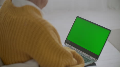 Mature-woman-nodding-her-head-yes-while-looking-at-a-green-screen-computer.-Elderly-mature-woman-with-gray-hair-and-a-video-call-on-her-Laptop.-Laptop-with-a-green-screen
