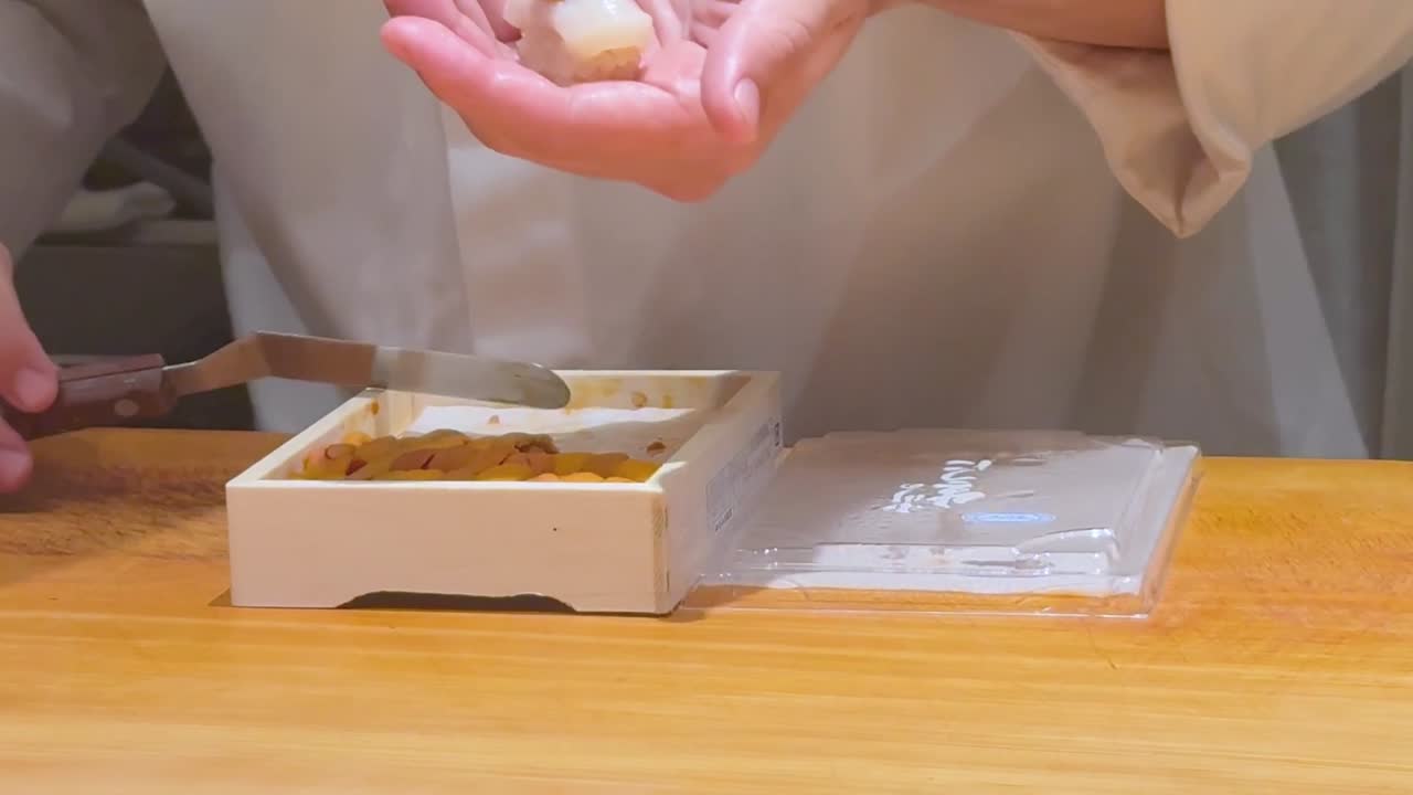 A chef skillfully adds uni to a rice ball using a small knife and steady hands.