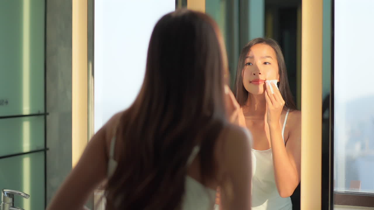 클렌저 병과 면 패드를 가진 젊은 아시아 소녀는 얼굴에서 화장품을 제거합니다.