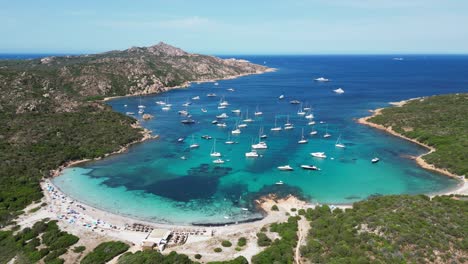 Barcos-Y-Yates-Flotando-En-La-Cala-Azul-Turquesa-En-La-Isla-De-La-Maddalena,-Cerdeña---4k-Aéreo-Dando-Vueltas