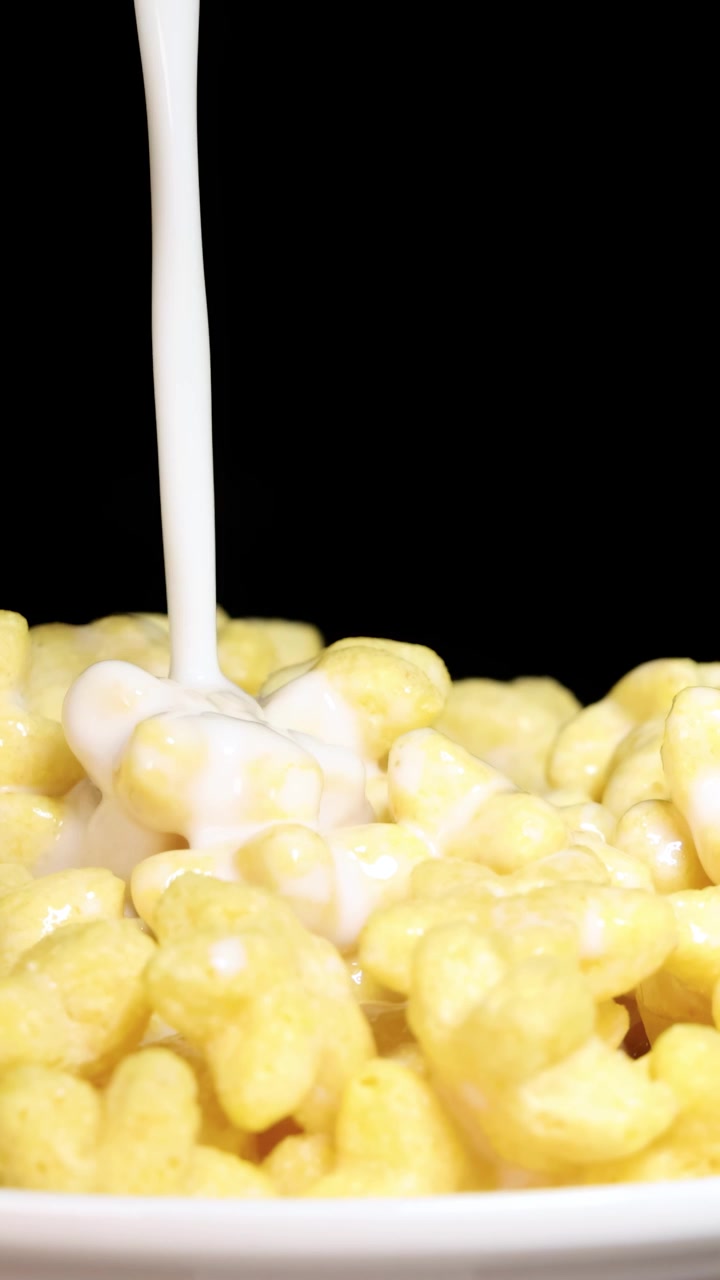 Il latte viene versato su cereali a forma di stella in una ciotola su sfondo nero, creando una dinamica scena per la colazione.
