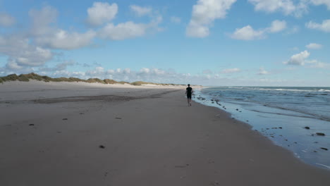 Forwards-tracking-of-man-jogging-on-sea-coast.-Sportsman-running-on-sand-beach-along-mild-waves.-Denmark