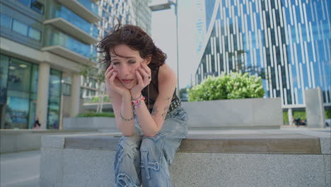 outdoor fashion portrait of young alternative style woman with tattoos and piercing sitting outside modern buildings shot in real time