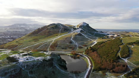 toma aérea de nieve en el asiento de arthur en edimburgo, volando sobre el lago dunsapie