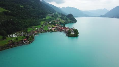 aerial view of iseltwald, showcasing a picturesque village on the shores of a turquoise lake, surrounded by lush green hills and mountains, with scattered houses and a serene, natural landscape