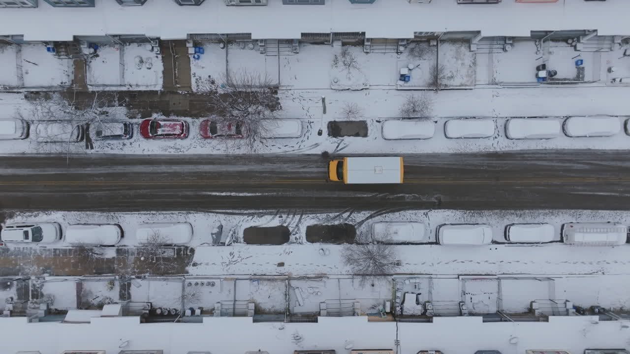 Top down aerial footage of a short school bus driving down a snow covered street in Philadelphia.