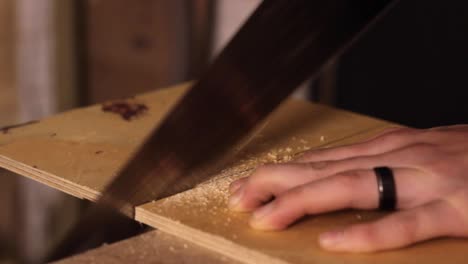 Carpenter-sawing-through-wood-using-their-hand-to-steady-the-plank