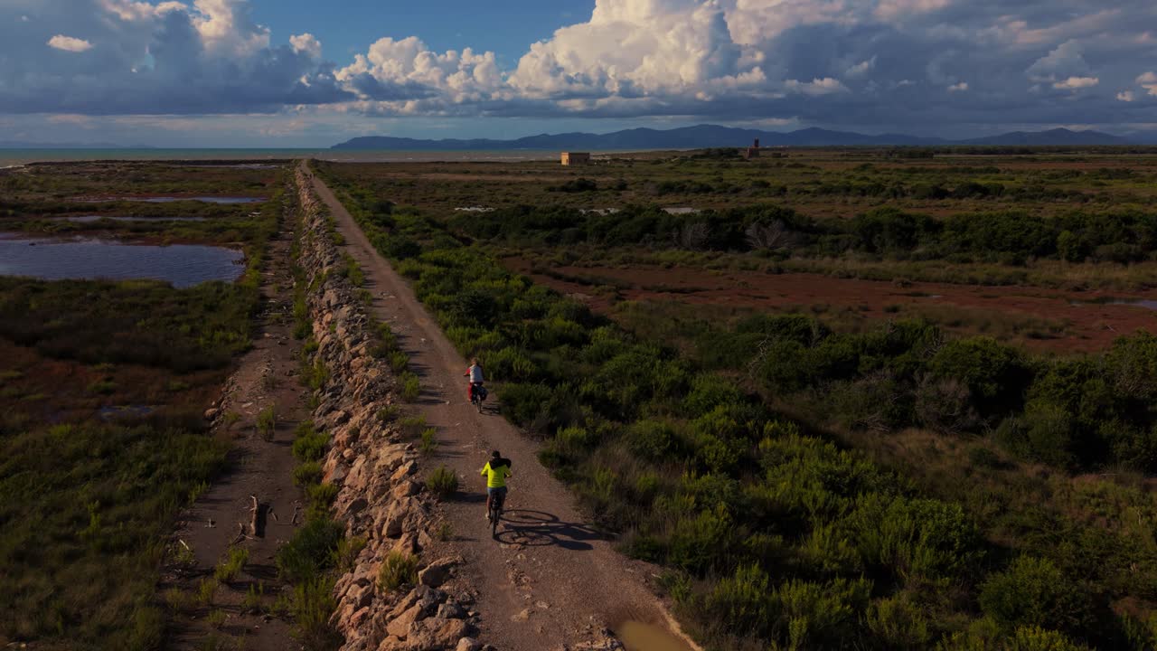 Active senior couple on electric bikes at Parco Maremma coastline with forested hills and blue sea