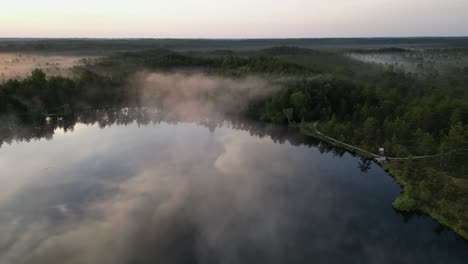 flyover of reflective foggy paukjarv lake in estonia at golden sunrise