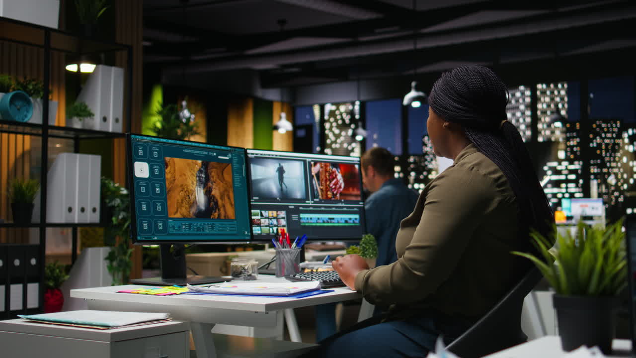 Young black woman video editor working with dual monitors in creative agency