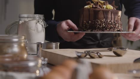 close up of man in kitchen at home putting freshly baked and decorated chocolate celebration cake onto work surface