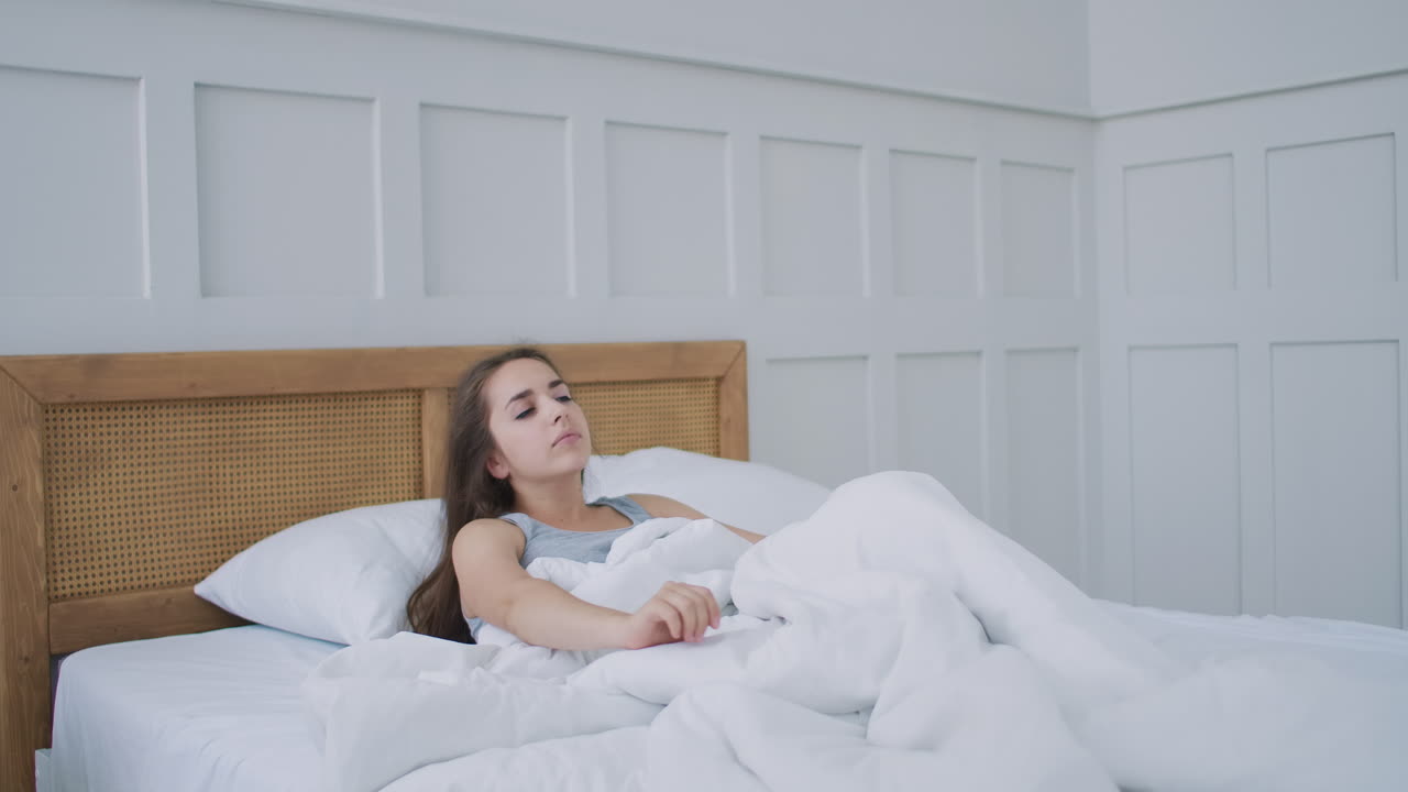 hermosa morena despertando lentamente por la mañana se estira y se levanta de la cama el sol brilla sobre ella desde la gran ventana. feliz joven saluda el nuevo día
