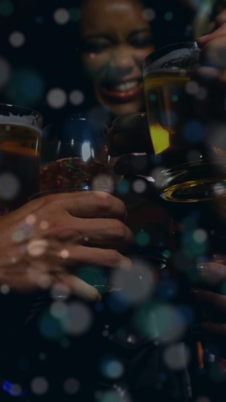 Video verticale: Una donna che alza una tazza e inizia un brindisi, gruppo al bar che fa tintinnare i boccali con effetto bokeh