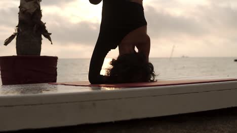 Woman-Standing-On-Head-In-Yoga-Pose-Salamba-Shirshasana-Outdoor,-Practicing-Yoga-Asana-On-Summer-Terrace-In-Front-The-Sea