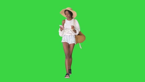 pretty african american woman in a straw hat texting on her phone while walking on a green screen, chroma key