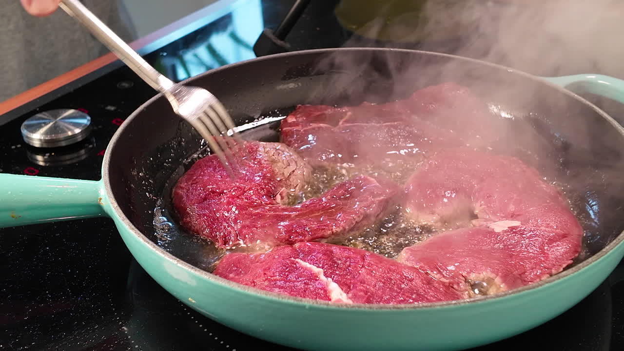 Pengambilan gambar close-up dari steak daging sapi yang dibalik dalam wajan penggorengan panas dengan minyak di atas kompor modern