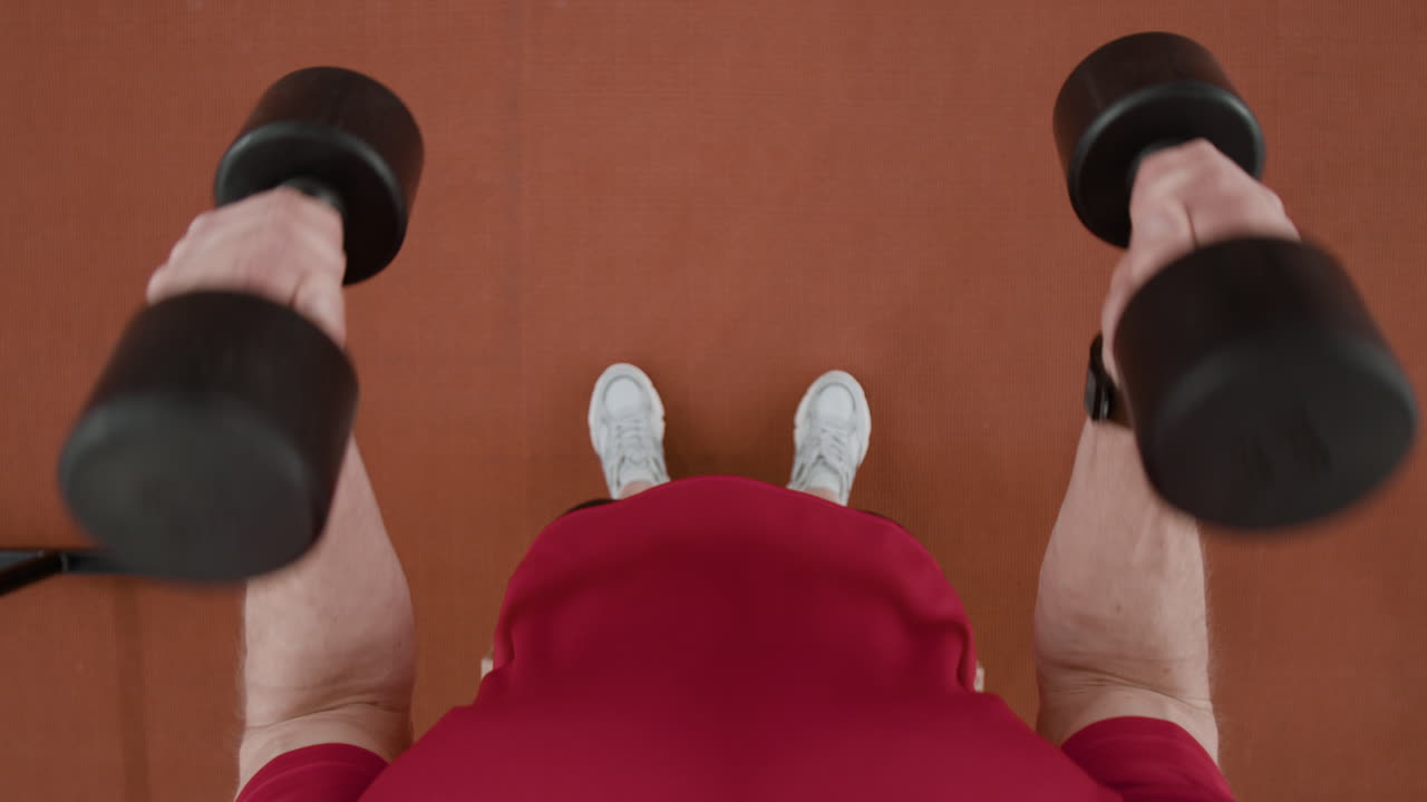Person lifting dumbbells in a gym, overhead view