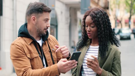 homme caucasien avec barbe et femme afro-américaine regardant quelque chose dans un smartphone dans la rue