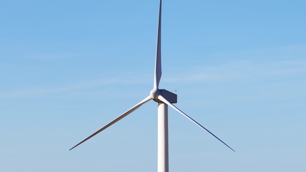 Primo piano di una turbina eolica che fa girare le sue pale contro un cielo azzurro limpido, generando elettricità pulita, rinnovabile e sostenibile per un futuro verde presso il parco eolico di Altamont Pass.
