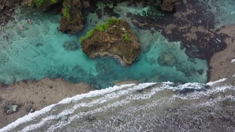 Meereswellen-Stürzen-Auf-Magpupungko-Gezeitenfelsenbecken-Mit-Menschen,-Die-Im-Klaren-Blauen-Wasser-Schwimmen