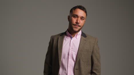 studio portrait of smiling mature male teacher wearing jacket standing against grey background shot in slow motion