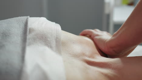 hands of wellness technician smoothing client chest and neck in slow circular massage motions on soft linen under bright clinical spa in tranquil treatment room with organized product trolley