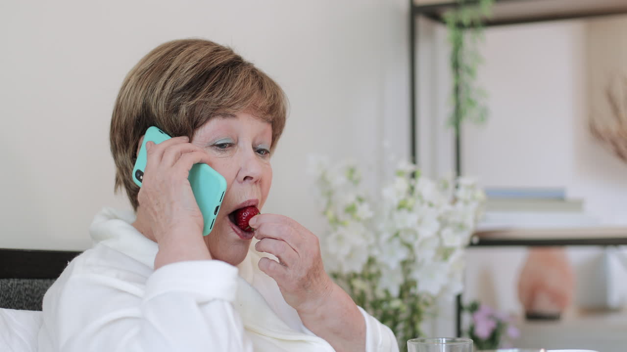 Elderly Woman Talking on Smartphone While Eating Strawberry