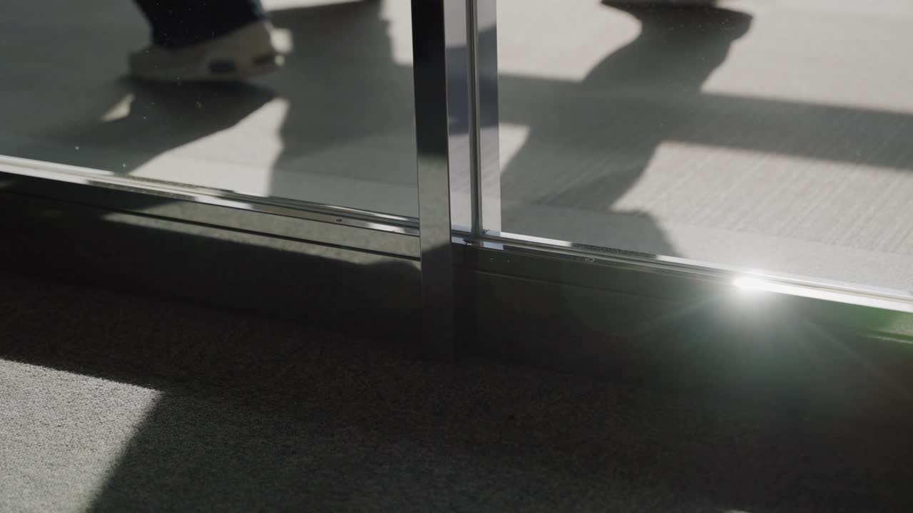 Shadows and silhouettes of people walking in line after boarding plane or disembarking entering airport terminal. Sunlight shining from glass windows in international airport as passengers pass by