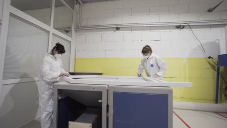 two women in protective gear working on wood in a manufacturing facility