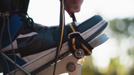 close-up of blue sneaker secured in stilt as hand tightens strap. details of black and yellow strap against metal frame highlight focus on adjustment. blurred outdoor background with natural light