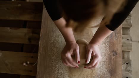 Top-footage-of-female-hands-with-beautiful-red-manicure-holding-clay-and-hardly-kneading-it-on-a-worktop.-Woman-wearing-beautiful-red-manicure