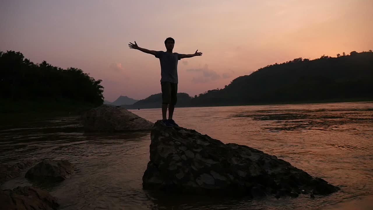 Person standing on a rock by the river at sunset